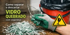 Mão com luva verde segurando vidro quebrado com balde vermelho ao fundo